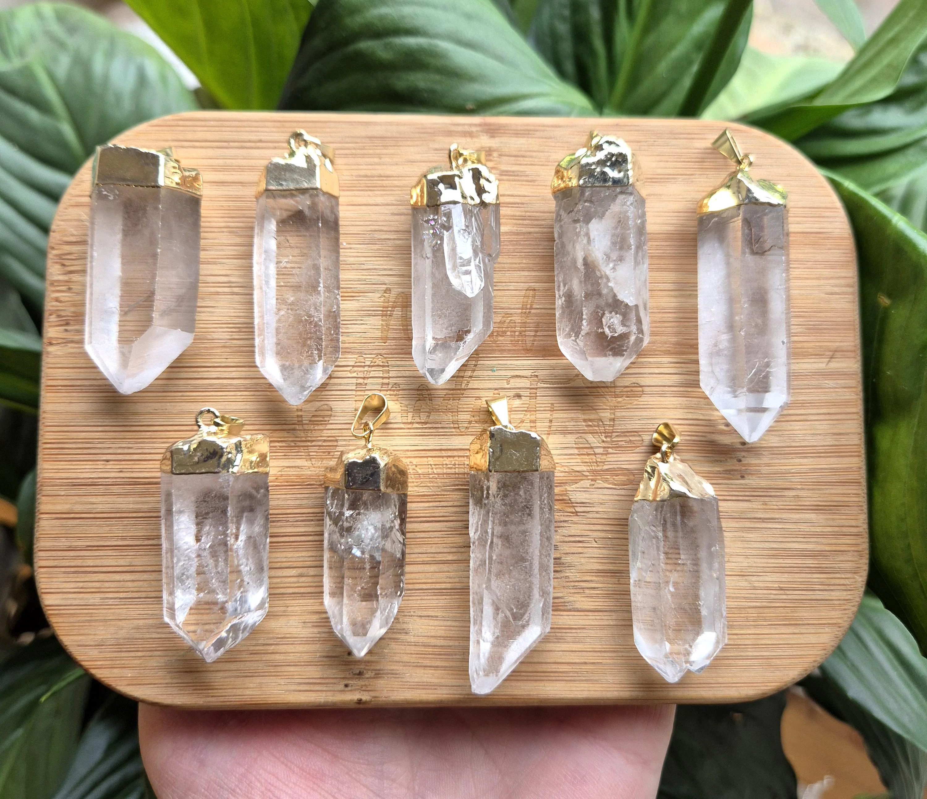 Eight clear quartz crystal points dipped in gold caps, displayed on a wooden board