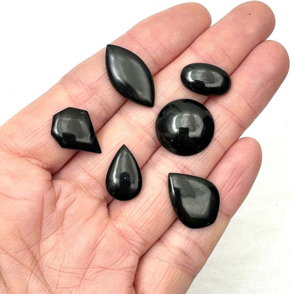 A hand holding six small, highly polished black gemstones of various shapes
