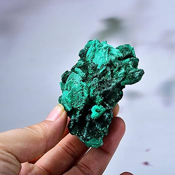 A hand holding a vibrant, raw cluster of dark green malachite mineral