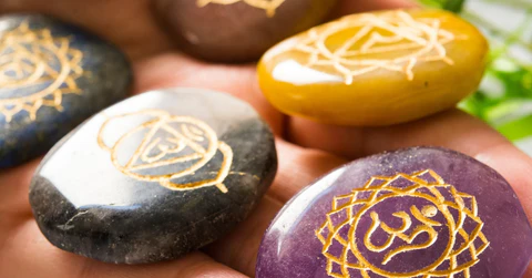 A hand holding several polished, colorful stones engraved with golden chakra symbols