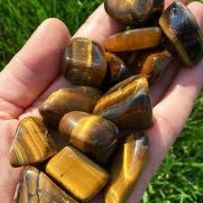 A hand holding a pile of tumbled, polished tiger's eye stones outdoors